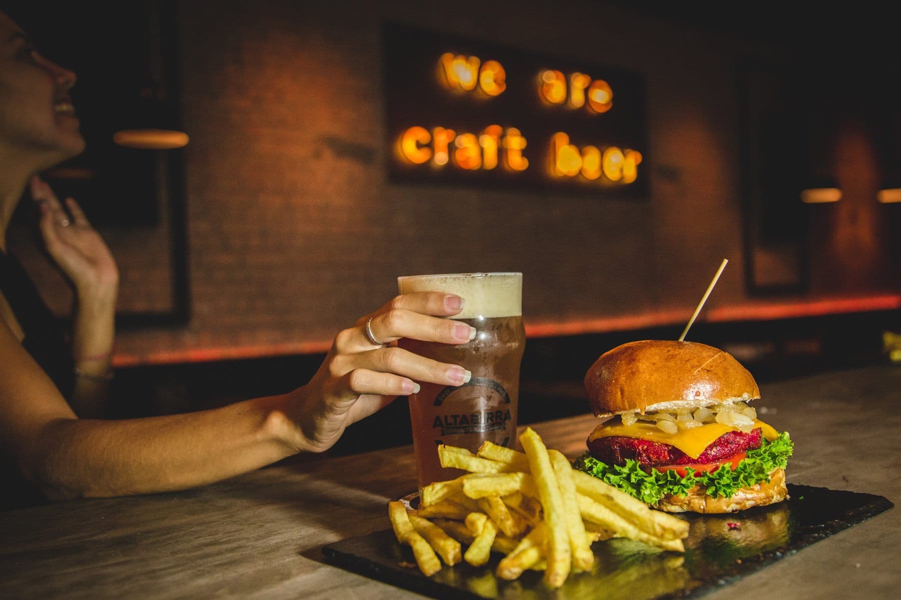 Burger y cerveza bajo el neón "we are craft beer"